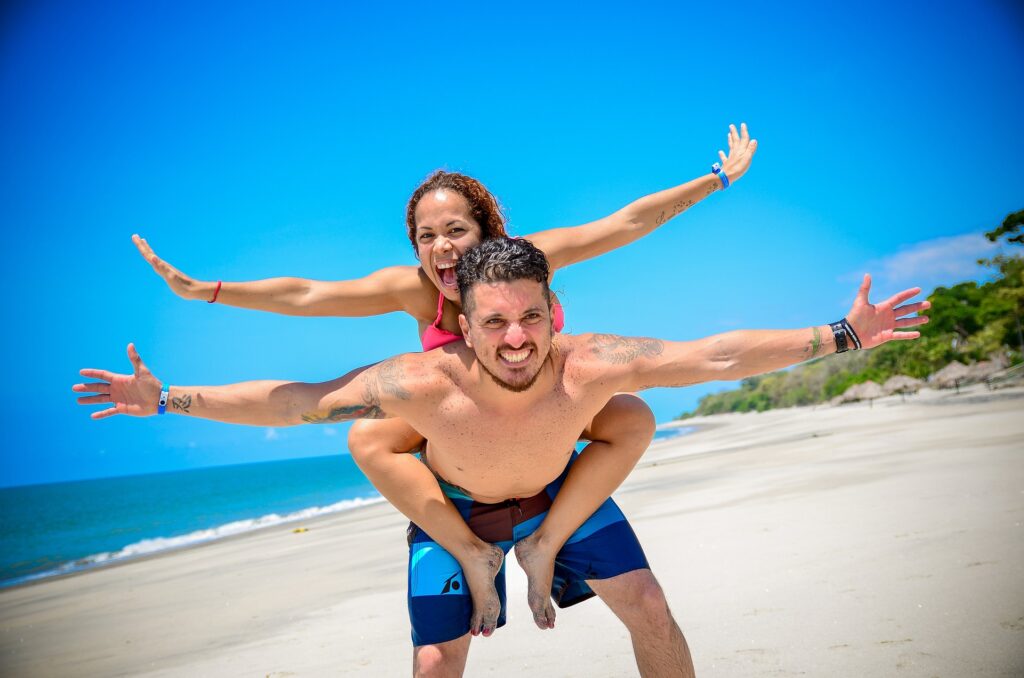 Child on her dad's back with arms out on the beach smiling