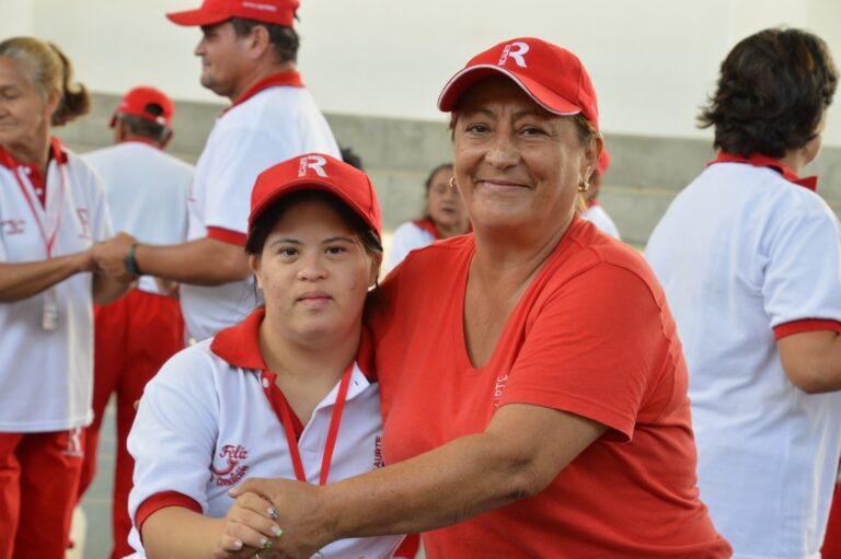 Woman holding hand of child with disability wearing red hats.